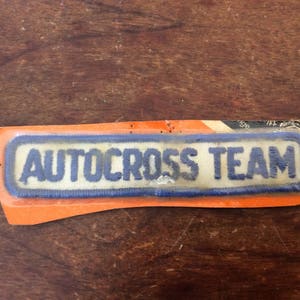 May include: A white patch with blue trim and the text "AUTOCROSS TEAM" on an orange background.