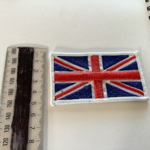 Puede incluir: Un parche bordado de la bandera del Reino Unido, con los colores rojo, blanco y azul. El parche está rodeado por un borde blanco.