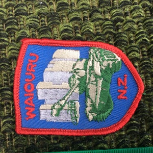 May include: Embroidered patch with a blue background and red border. The patch features the word "WAIORU" in red, along with a green and white illustration and the letters "N.Z." The patch is rectangular with a pointed end.