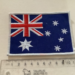 Könnte beinhalten: Ein gestickter Aufnäher der australischen Flagge. Die Flagge zeigt ein rotes Kreuz mit weißen Sternen auf blauem Hintergrund.