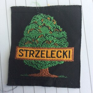Pode incluir: Um remendo bordado preto com uma árvore verde e uma faixa marrom que diz "STRZELECKI".