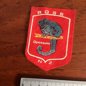 May include: Red felt patch with a white border, featuring a blue possum on a branch with the text "ROSS" at the top and "Opossum" and "NZ" at the bottom.