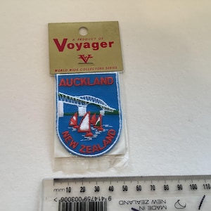 Könnte beinhalten: Auckland, Neuseeland-Patch aus der Voyager World Wide Collectors Series. Der blaue Patch zeigt eine Brücke, Segelboote und den Stadtnamen. Der Patch befindet sich in einer transparenten Plastikhülle.
