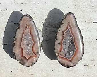 May include: Two agate slices with pink and white banding and a clear center. The slices are smooth and polished.