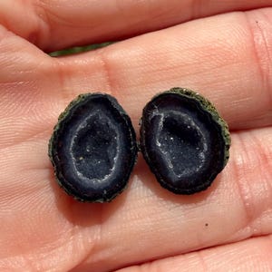 May include: Two dark blue geode halves with a sparkling crystal interior and a rough, green-brown exterior. The geode halves are displayed against a neutral background.