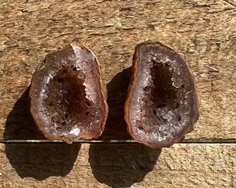 May include: Two halves of a geode with a purple and white crystal interior. The geode halves are brown on the outside and have a rough, natural texture.