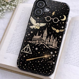 May include: Black phone case with gold illustrations of a castle, owl, glasses, and stars. The case features a wand, lightning bolt, and moon design. The case is resting on an open book.
