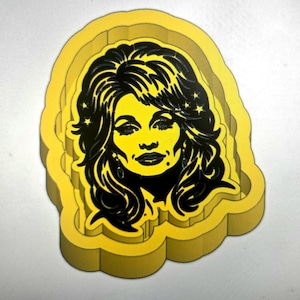 May include: A yellow cookie cutter featuring a raised, stylized portrait of a person with voluminous hair, defined facial features, and small star accents integrated into the hair design, with a thick, molded border surrounding the central image.