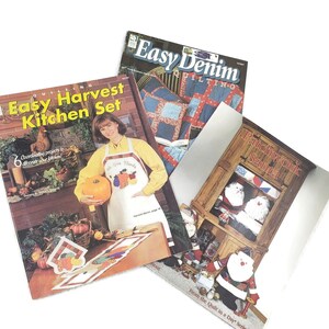 May include: Three quilting pattern books with colorful covers. The first book is titled "Easy Denim Quilting" and features a red, white, and blue quilt. The second book is titled "Easy Harvest Kitchen Set" and features a woman holding a pumpkin and a fall-themed kitchen scene. The third book is titled "Patchwork Santa" and features a Santa Claus figure made of patchwork fabric.