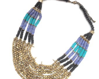 May include: A multi-strand necklace with black, blue, and turquoise beads. The necklace has a gold metal clasp and a gold metal design in the center.