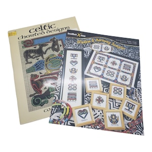 May include: Two cross-stitch pattern books. One titled "Celtic Charted Designs" with images of Celtic knotwork and animals. The other, "Wisdom & Harmony Sampler," features framed cross-stitch designs with geometric and floral patterns.