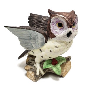 May include: A porcelain owl figurine with brown, white, and blue markings. The owl is perched on a branch with green leaves and red berries.