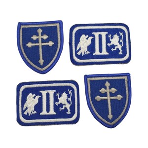 May include: Four embroidered patches with a blue background and white stitching. Two patches feature a white cross with a white eagle and lion on either side of a white Roman numeral II. The other two patches feature a white cross inside a shield shape.