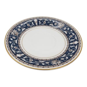 May include: White ceramic saucer with a navy blue and gold floral design. The saucer has a gold rim and a central indentation for a teacup. The floral pattern includes white and brown accents.
