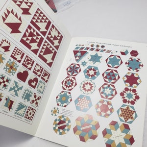 Puede incluir: Un libro con instrucciones para crear bloques de colcha usando tri&aacute;ngulos, diamantes, cuadrados y hex&aacute;gonos. El libro presenta una variedad de dise&ntilde;os de bloques de colcha coloridos con esquemas de colores rojo, blanco y azul.