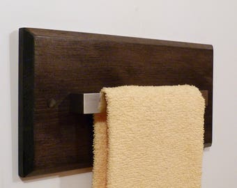 May include: A dark brown wooden towel rack with a silver metal bar. A light yellow towel is hanging on the bar.