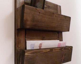 May include: A dark brown wooden wall organizer with two shelves and a key hook rack. The top shelf has a small compartment for a phone. The middle shelf is for mail and the bottom shelf has a key hook rack.