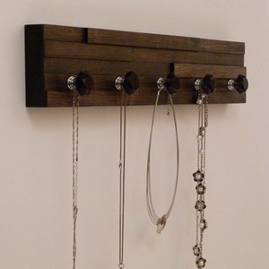 May include: A dark brown wooden jewelry organizer with black knobs and five silver chains hanging from the knobs.