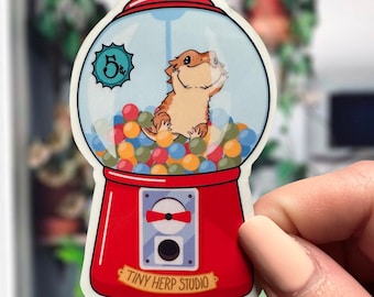 May include: A red and white gumball machine with a bearded dragon inside. The gumball machine has a sign that says "5c" and "Tiny Herp Studio".