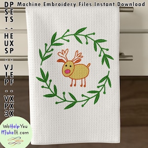 以下が含まれることがあります： 白いキッチンクロスに、緑色のリースと黄色のトナカイが刺繍されています。トナカイは赤い鼻と角を持っています。