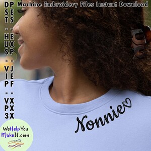 Op de afbeelding: Een lichtblauw sweatshirt met de naam "Nonnie" geborduurd in zwarte cursieve letters met een klein hartje aan het einde.