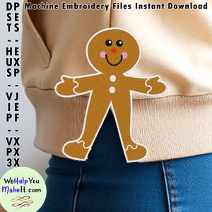 May include: A brown gingerbread man embroidery design with white details, including a smile, eyes, and buttons. The design is on a beige sweatshirt with blue jeans.