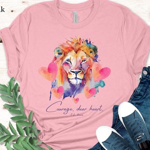 May include: Pink t-shirt with a watercolor illustration of a lion's head surrounded by pink hearts. The text "Courage, dear heart." is printed below the lion with the words "C.S. Lewis" in smaller font below the text.