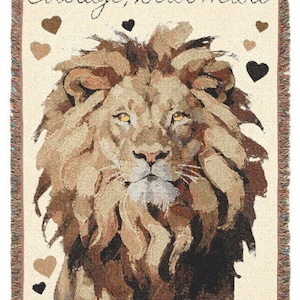 May include: Woven throw blanket featuring a lion's face with a mane of brown and tan hues. The words "Courage, Dear Heart" are written in script above the lion. Brown and black heart shapes are scattered around the lion.