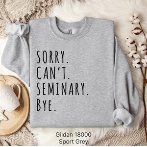 Op de afbeelding: Grijs sweatshirt met de tekst "SORRY. CAN'T. SEMINARY. BYE." gedrukt op de voorkant. Gildan 18000 Sport Grey.