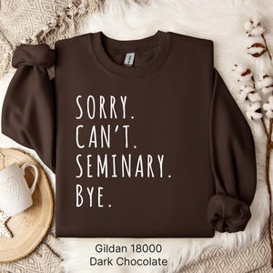 Op de afbeelding: Een donkerbruin sweatshirt met de tekst "Sorry. Can't. Seminary. Bye." in witte letters. Het sweatshirt is gemaakt door Gildan en is maat 18000.