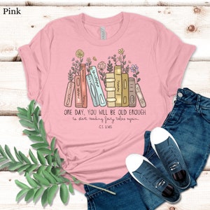 May include: Pink t-shirt with a graphic of a stack of books with flowers and the quote "ONE DAY, YOU WILL BE OLD ENOUGH to start reading fairy tales again. -C.S. LEWIS"