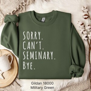 Op de afbeelding: Een groen Gildan 18000 sweatshirt met de tekst "Sorry. Can't. Seminary. Bye." in wit gedrukt.