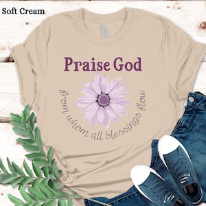 May include: A beige t-shirt with a purple daisy graphic and the text "Praise God from whom all blessings flow".