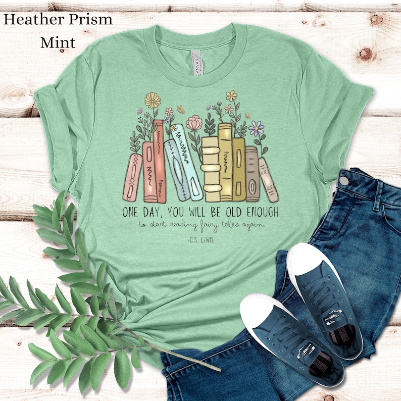 May include: A light green t-shirt with a stack of books and flowers. The text on the shirt reads "ONE DAY, YOU WILL BE OLD ENOUGH to start reading fairy tales again - C.S. LEWIS"
