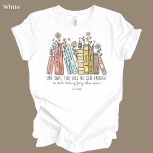 May include: White t-shirt with a graphic of a stack of books with flowers and the quote "ONE DAY, YOU WILL BE OLD ENOUGH to start reading fairy tales again - C.S. LEWIS"