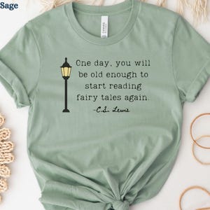 May include: Sage green t-shirt with the quote "One day, you will be old enough to start reading fairy tales again." by C.S. Lewis. The design includes a black and yellow illustration of a lamppost.