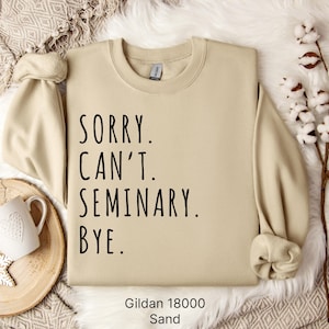 Op de afbeelding: Een beige sweatshirt met de tekst "Sorry. Can't. Seminary. Bye." in zwarte letters. Het sweatshirt is gemaakt door Gildan en is in de kleur Zand.
