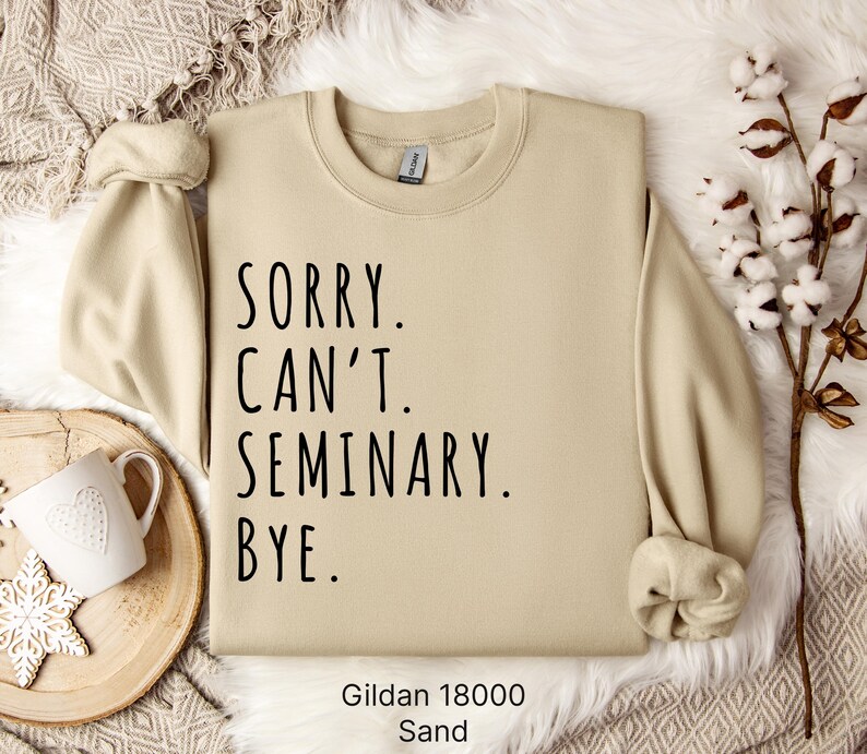 Op de afbeelding: Een beige sweatshirt met de tekst "Sorry. Can't. Seminary. Bye." in zwarte letters. Het sweatshirt is gemaakt door Gildan en is in de kleur Zand.