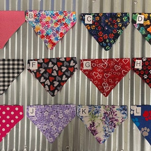 May include: Twelve different dog bandanas with various patterns, including polka dots, hearts, flowers, paw prints, and bones. The bandanas are arranged in two rows of six, with each bandana labeled with a letter from A to L.