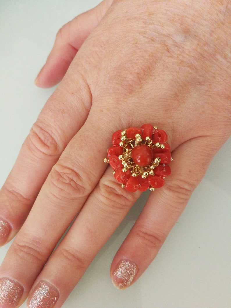 May include: A gold ring with a large red coral flower design. The coral is arranged in a cluster of small, round pieces.