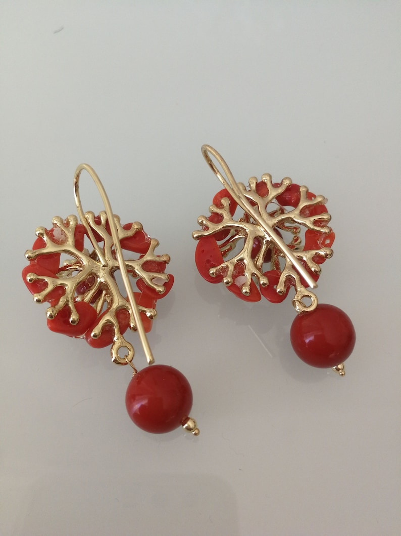 May include: A pair of gold earrings with red coral branches and red coral beads hanging from the bottom.