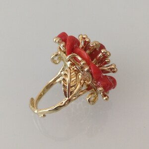 May include: A gold ring with a red coral flower design. The ring is set with a single red coral stone in the center of the flower.