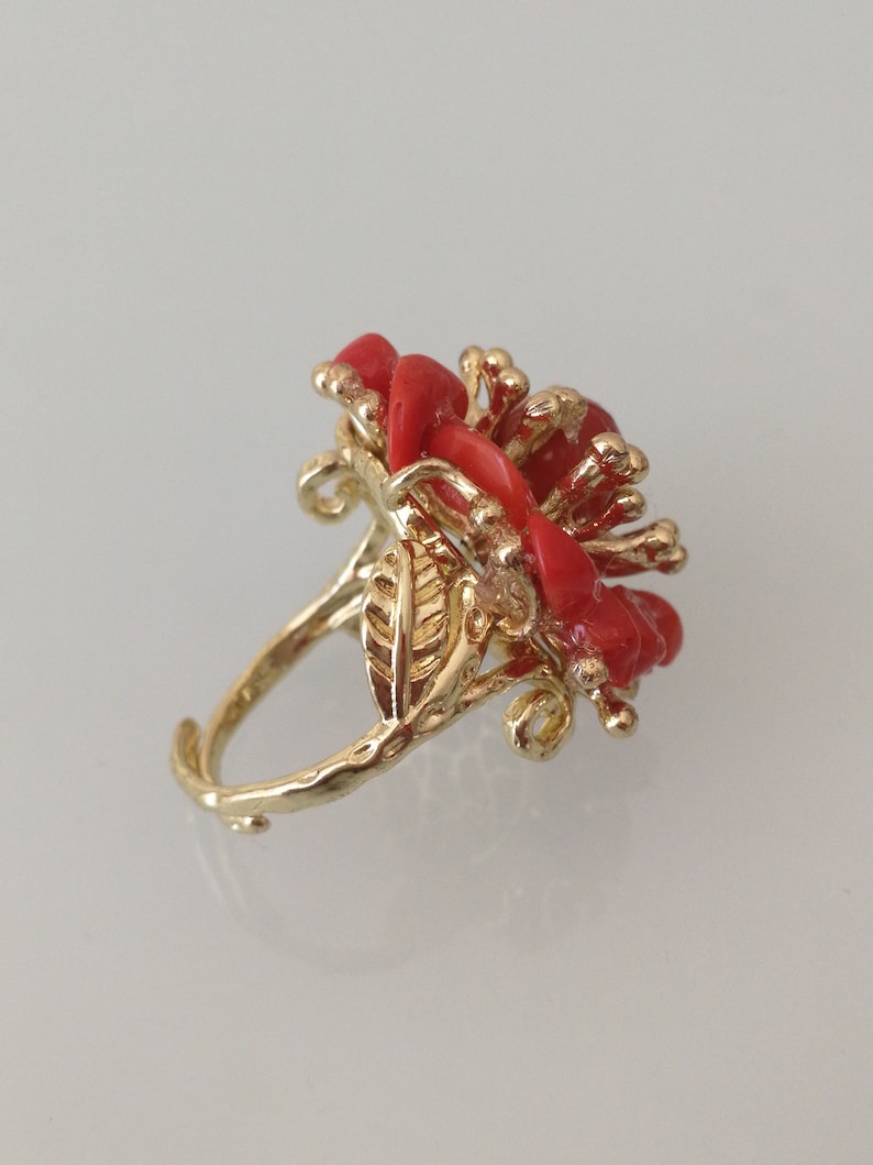 May include: A gold ring with a red coral flower design. The ring is set with a single red coral stone in the center of the flower.