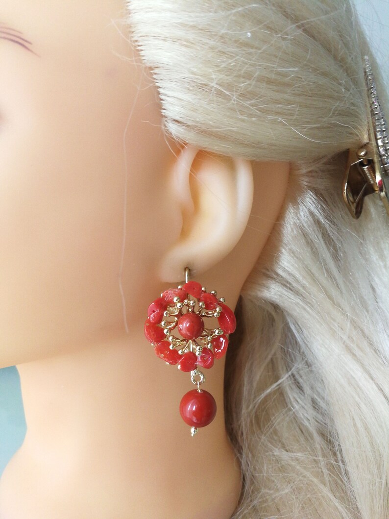 May include: Coral earrings with a gold-toned flower design and a single coral bead dangling from the bottom.