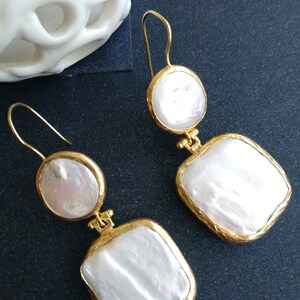 May include: A pair of gold earrings with white pearl drops. The earrings have a square and round shape.