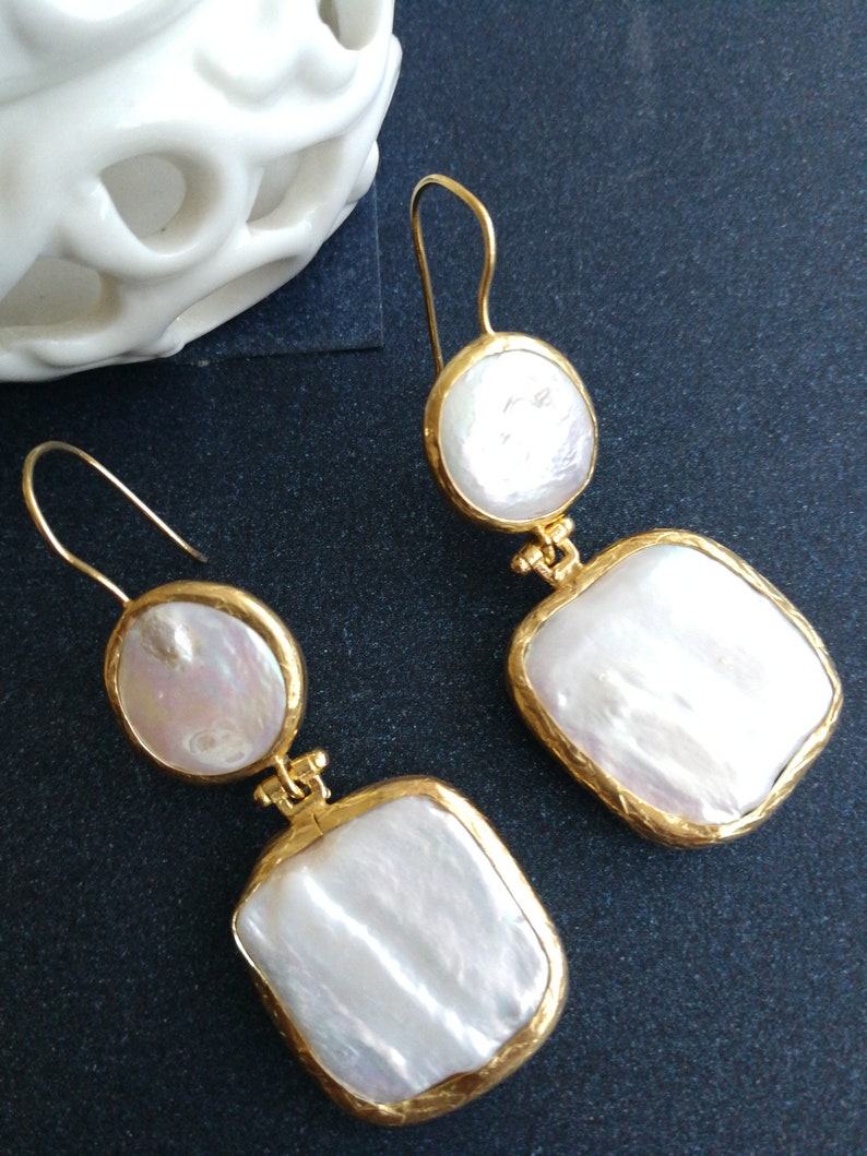 May include: A pair of gold earrings with white pearl drops. The earrings have a square and round shape.