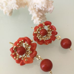 May include: A pair of coral earrings with gold accents. The earrings are made of small pieces of coral that are arranged in a flower shape. The earrings have a drop design with a round coral bead hanging from the flower.