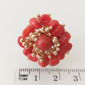 May include: A coral ring with a large red coral center surrounded by smaller coral pieces and gold accents. The ring measures approximately 1 inch in diameter.
