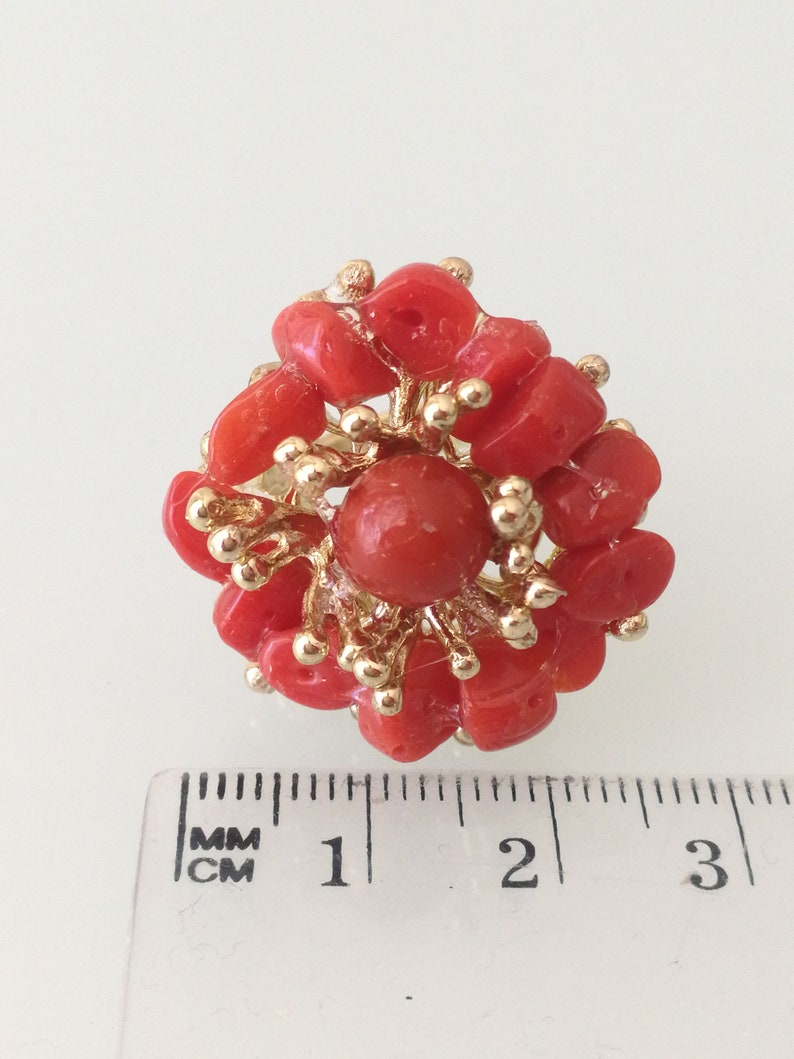 May include: A coral ring with a large red coral center surrounded by smaller coral pieces and gold accents. The ring measures approximately 1 inch in diameter.