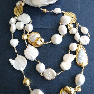 May include: A multi-strand necklace with large white baroque pearls and gold accents. The necklace features a variety of pearl shapes and sizes, including round, oval, and irregular.